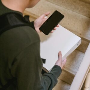 A delivery person checking their phone while holding a package on the stairs.