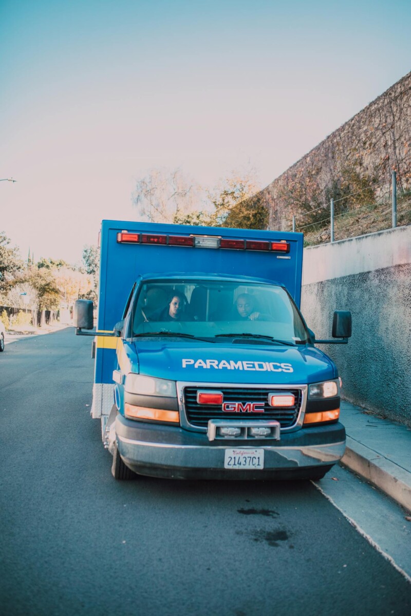Front view of a parked blue paramedic ambulance on a sunny roadside.
